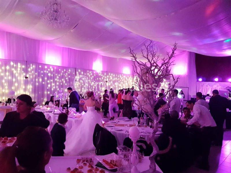 Salle de réception décorée avec des lumières tamisées, des invités assis et debout, et une mariée en robe blanche.