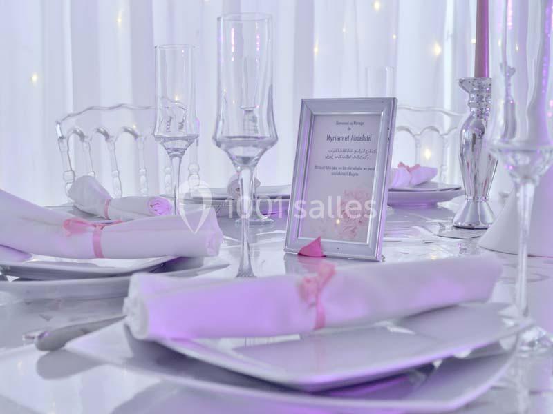 Table élégamment dressée avec nappes blanches, serviettes pliées, verres et cadre photo décoratif.