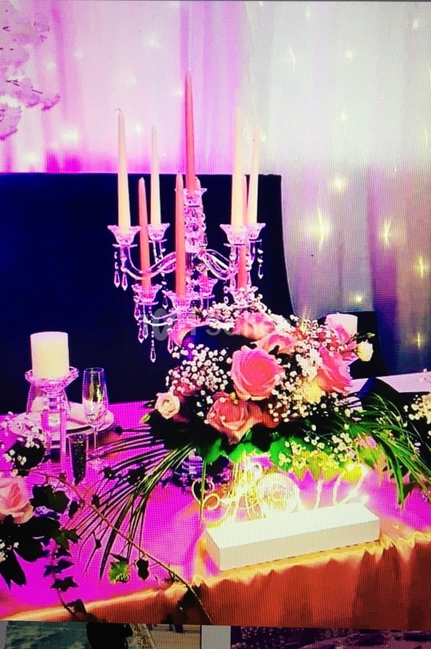 Table décorée avec des roses, un chandelier argenté, des bougies et un éclairage rose en arrière-plan.