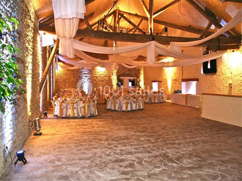 Salle de réception décorée avec des tables rondes dressées, des chaises ornées de rubans dorés et des voilages suspendus.