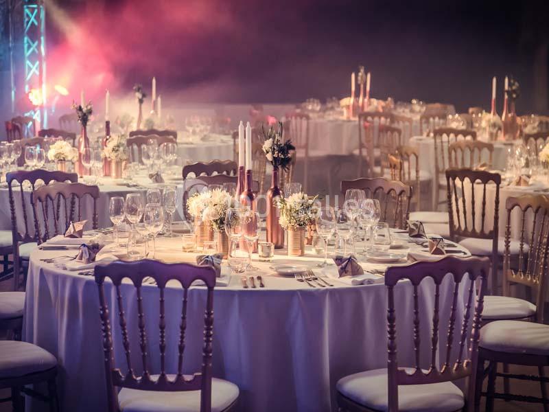 Salle de réception décorée avec des tables rondes élégantes, bougies, fleurs et vaisselle raffinée.