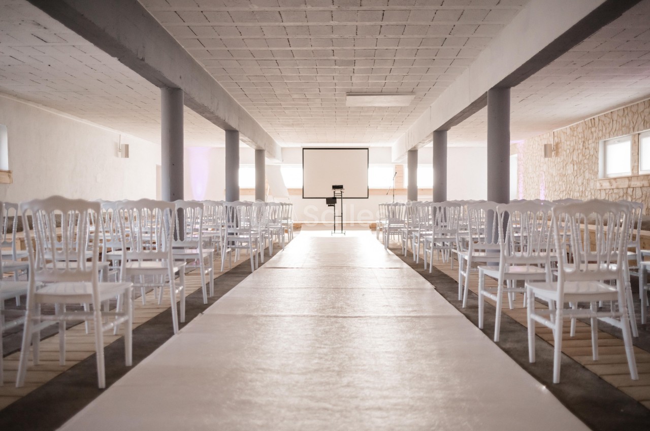 Salle lumineuse avec rangées de chaises blanches alignées face à un écran de projection.