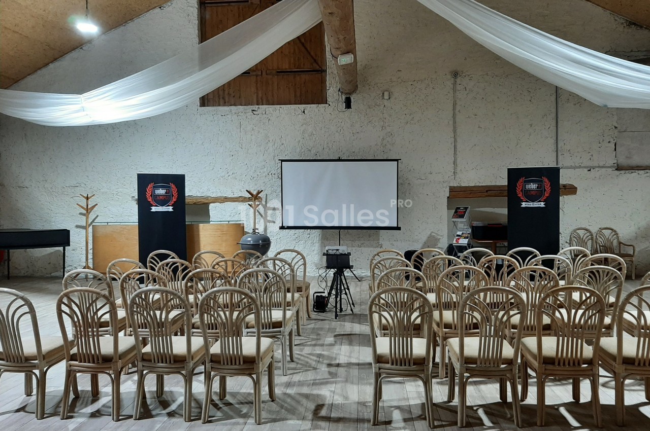 Salle de conférence avec chaises alignées, écran de projection, projecteur et décoration sobre sous un plafond en bois.