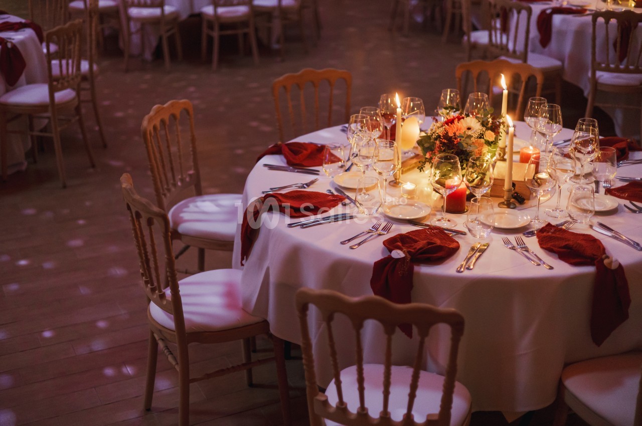 Table ronde élégamment dressée avec nappes blanches, serviettes rouges, bougies et centre de table floral.