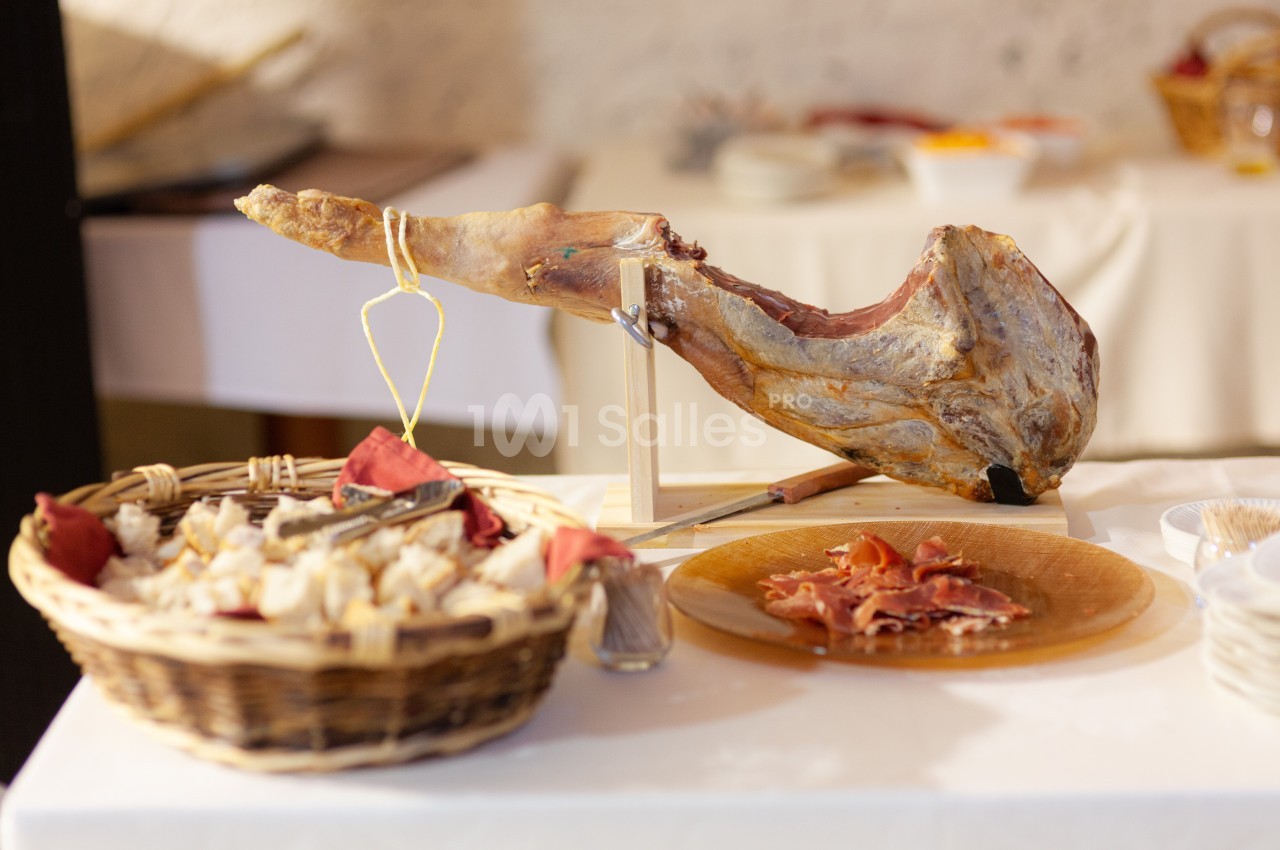 Jambon entier sur support avec tranches coupées, accompagné d'un panier de pain sur une table blanche.