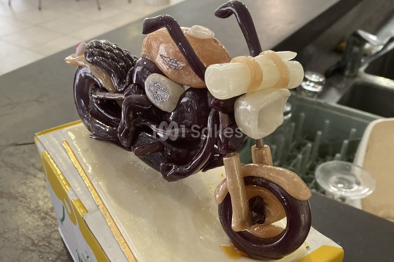 Sculpture miniature d'une moto réalisée en sucre coloré, exposée sur un socle dans un environnement intérieur.