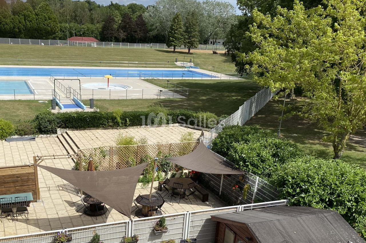 Vue d'une terrasse ombragée avec des voiles, donnant sur une piscine extérieure et un espace vert arboré.