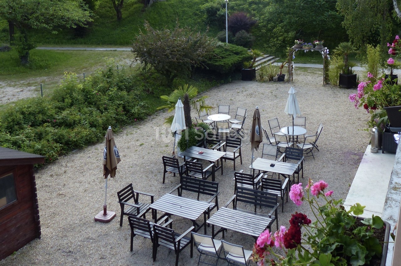 Terrasse extérieure avec tables et chaises en métal, entourée de verdure et décorée de fleurs.