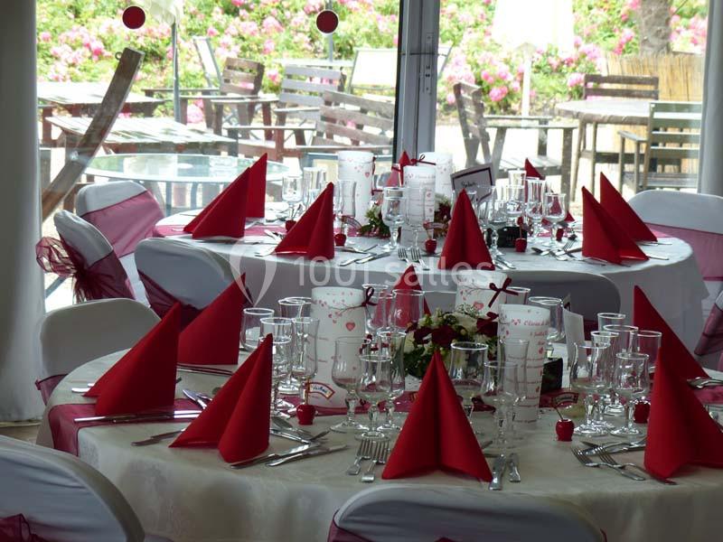 Tables dressées pour un événement, avec nappes blanches, serviettes rouges pliées et décorations florales.