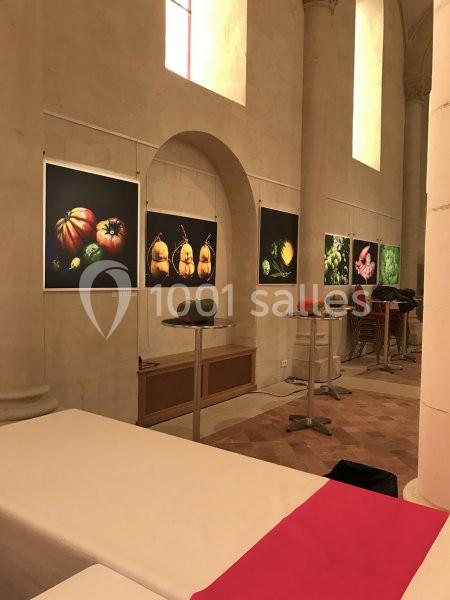 Exposition de photographies de légumes colorés accrochées sur les murs d'une salle aux colonnes en pierre.