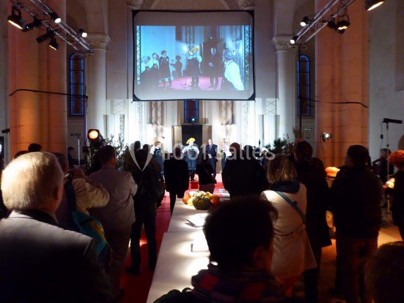 Personnes rassemblées dans une salle éclairée, regardant une projection sur grand écran lors d'un événement.
