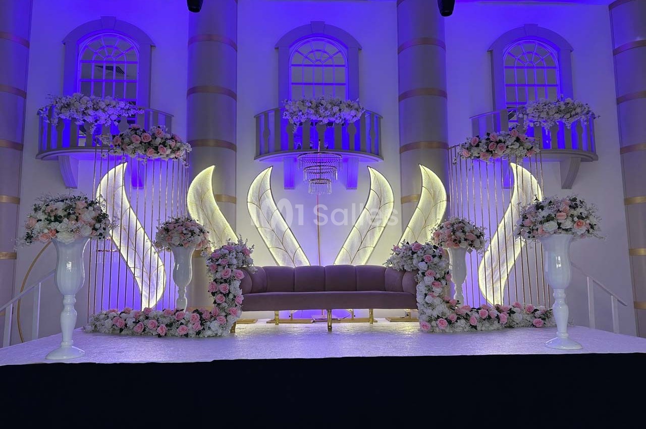 Décor de scène élégante avec canapé central, fleurs blanches et roses, éclairage violet et arches lumineuses.