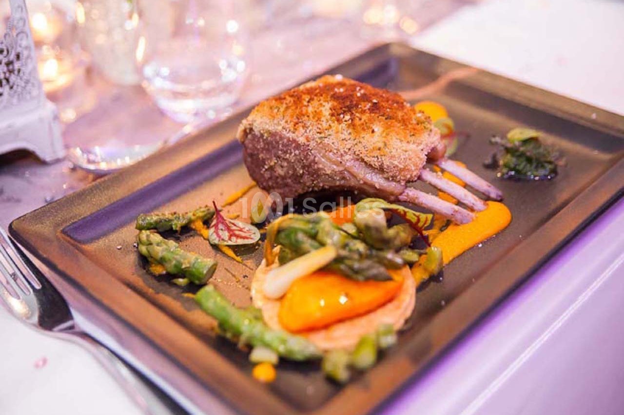 Carré d'agneau rôti avec purée de carottes, asperges et tartelette de légumes, servi sur une assiette élégante.