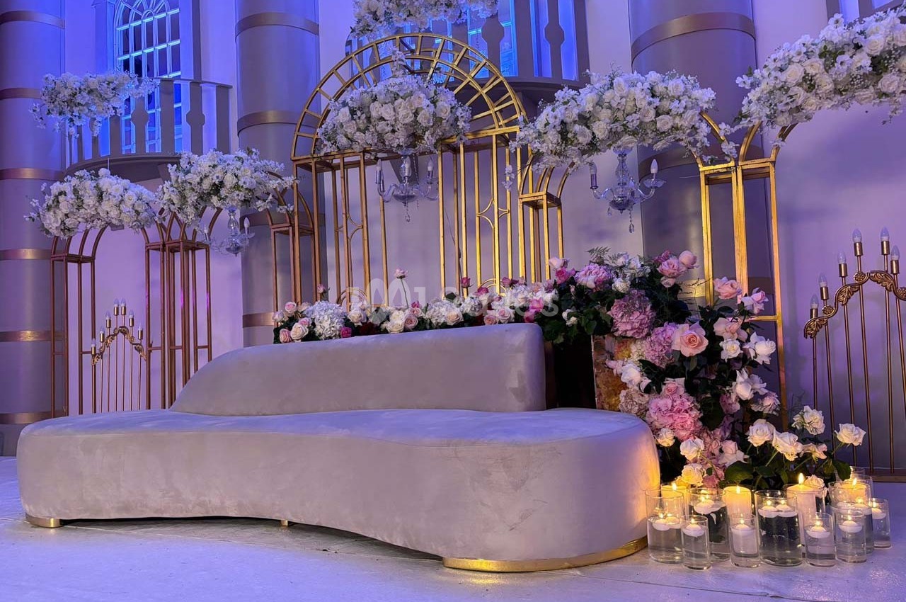 Décor élégant avec canapé gris, arches dorées, fleurs blanches et roses, et bougies dans un cadre lumineux.