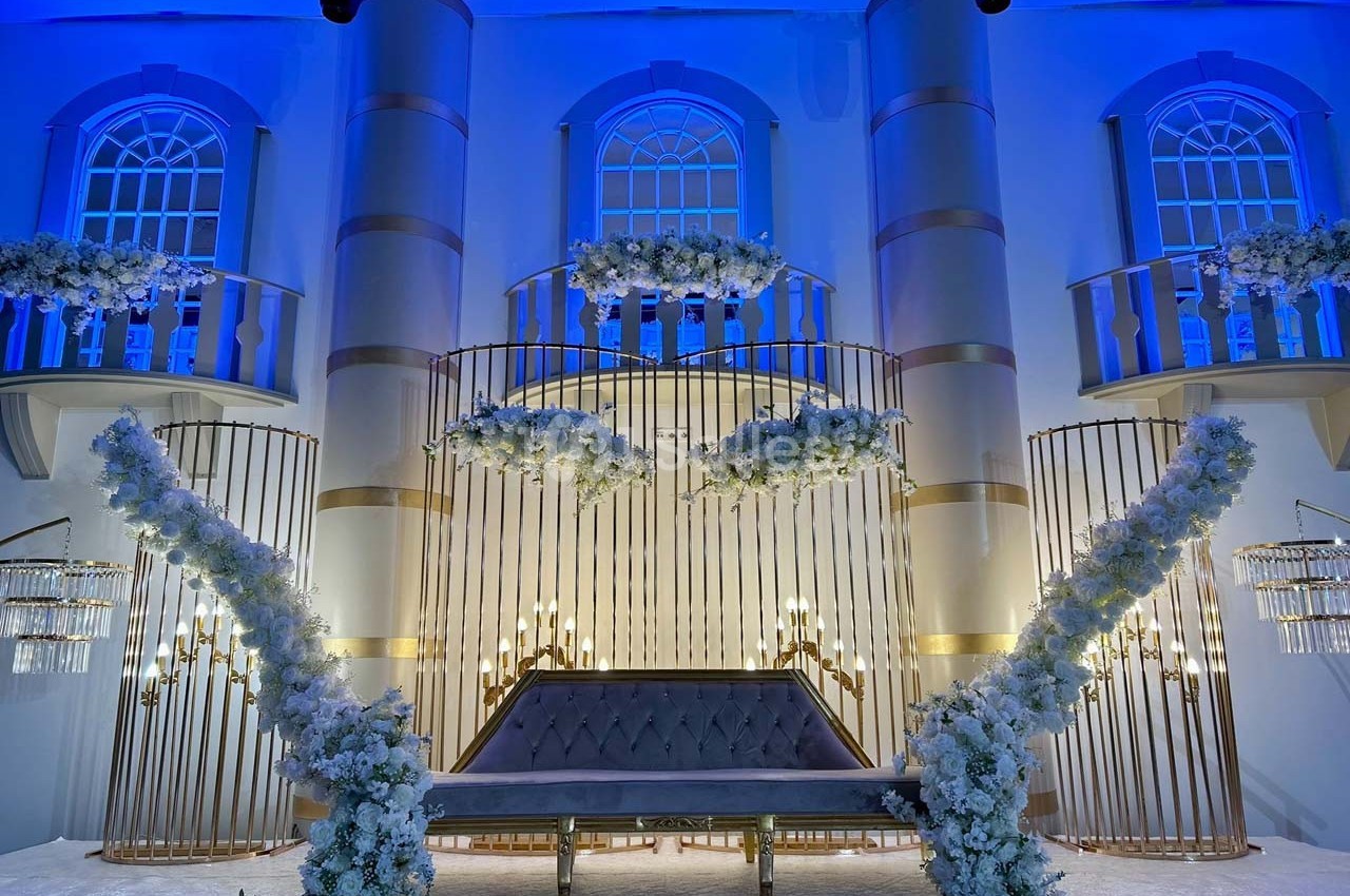 Décor de mariage avec arche dorée, fleurs blanches et éclairage bleu dans une salle élégante.