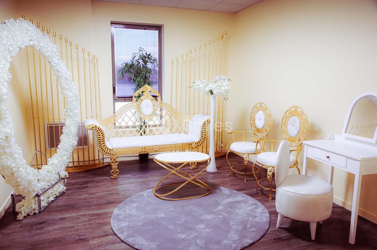 Salle lumineuse avec mobilier doré et blanc, comprenant un canapé, des chaises, une coiffeuse et un décor floral.