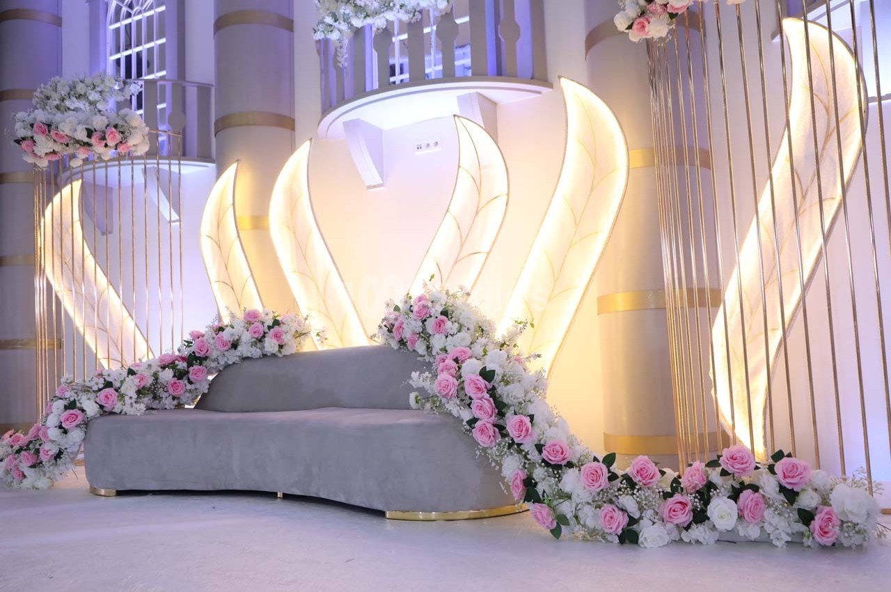 Décor lumineux avec un canapé gris entouré de fleurs roses et blanches, devant des structures dorées et éclairées.