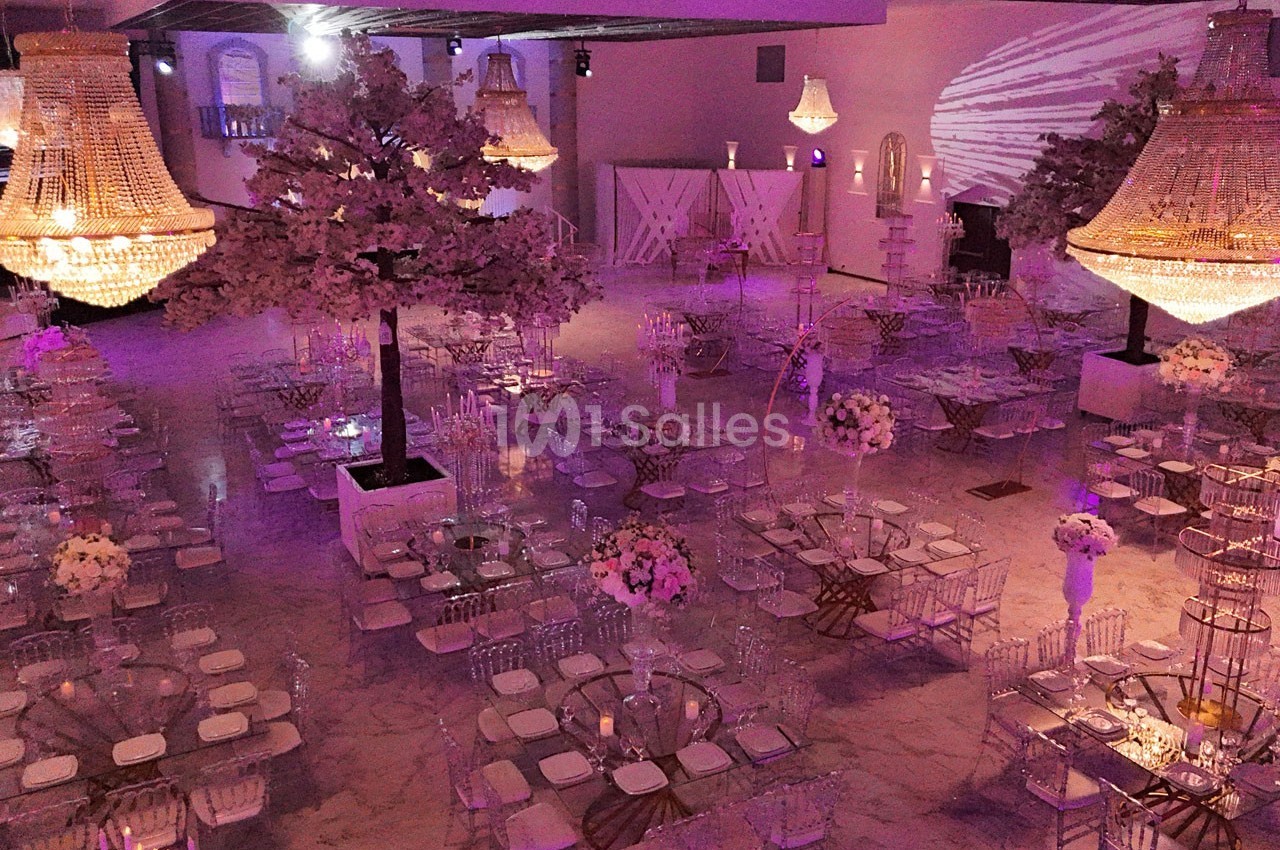 Salle de réception décorée avec des tables élégantes, des chandeliers imposants et des arbres artificiels illuminés.