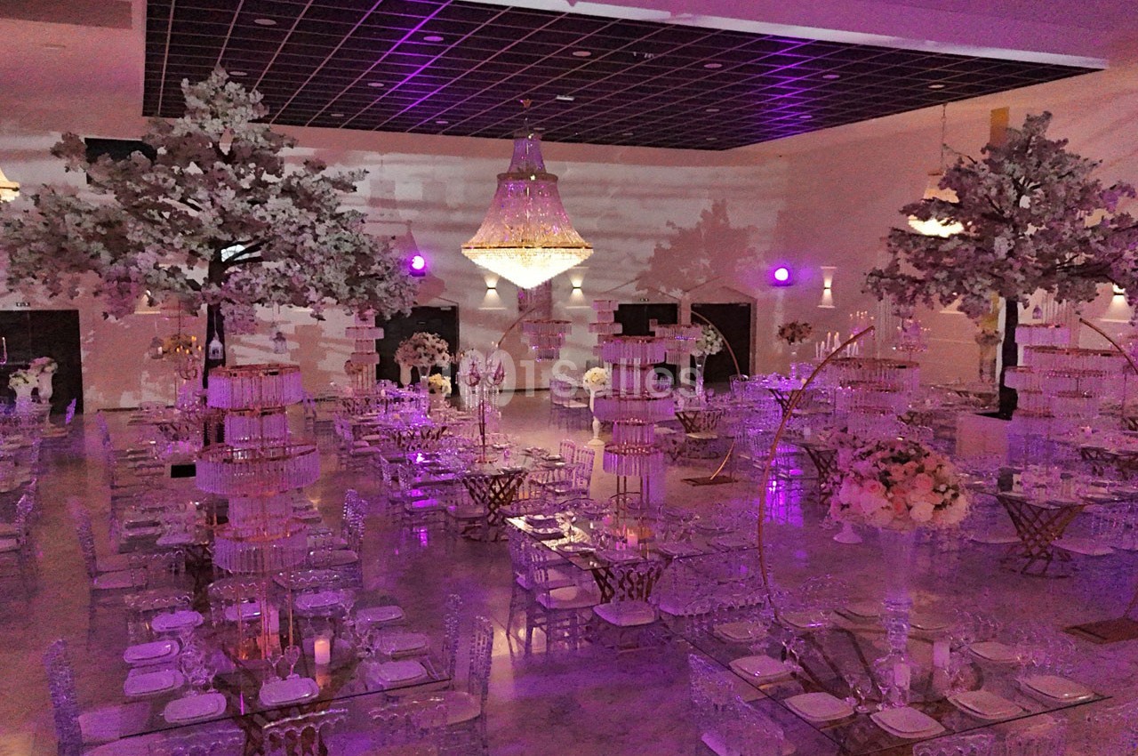 Salle de réception décorée avec des tables élégantes, des arbres artificiels et un éclairage violet tamisé.