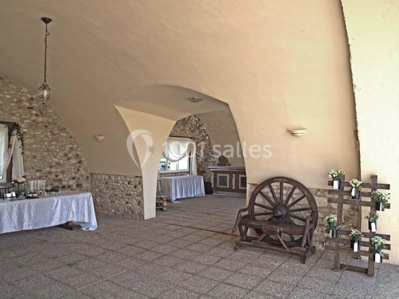 Salle voûtée en pierre avec des tables décorées, une roue en bois et des arrangements floraux sur un support en bois.