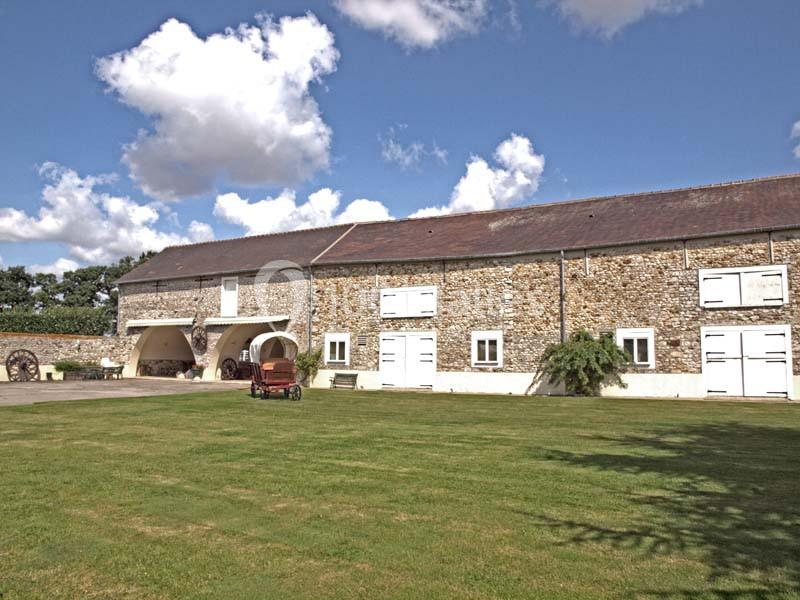 Bâtiment en pierre avec des volets blancs, une cour herbeuse et un ciel partiellement nuageux.