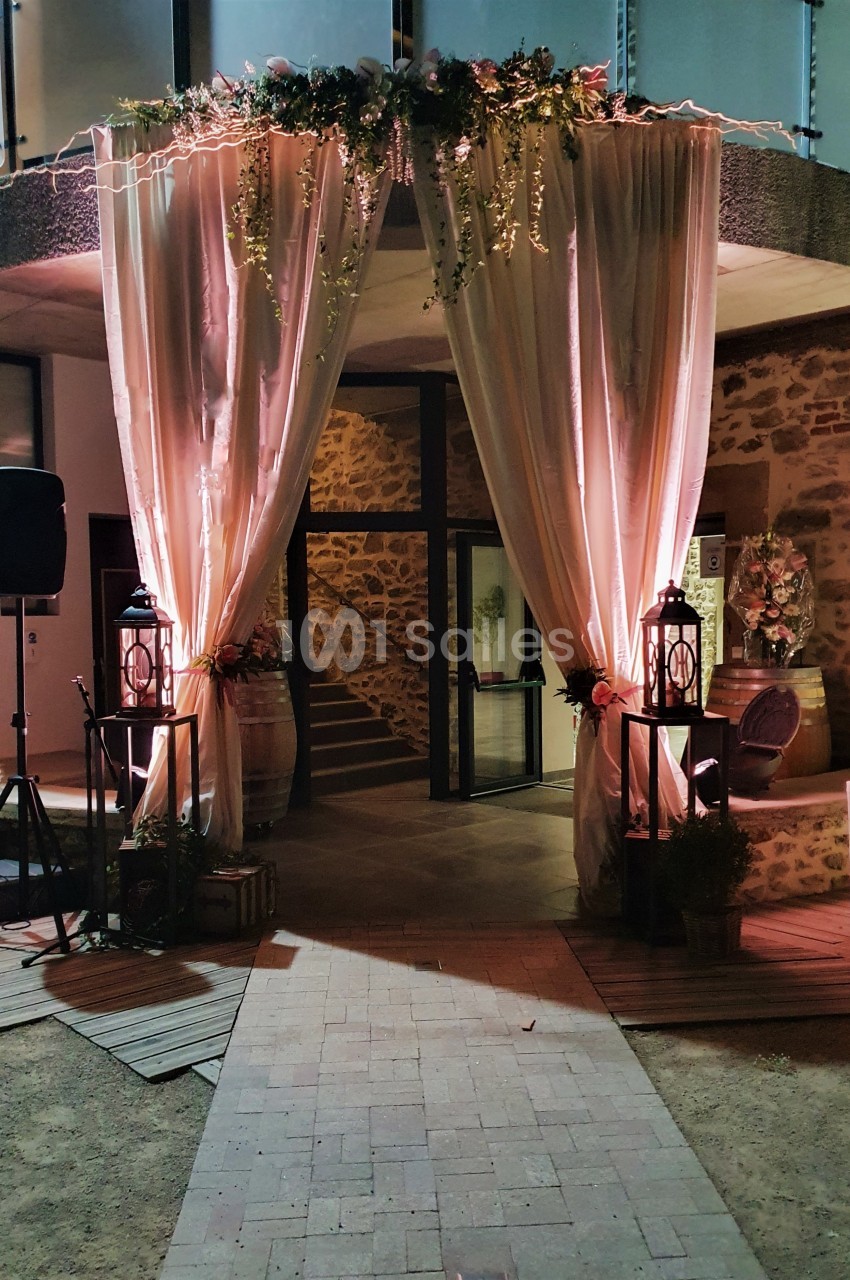 Entrée décorée avec des rideaux roses, guirlandes lumineuses et lanternes, menant à un espace intérieur en soirée.