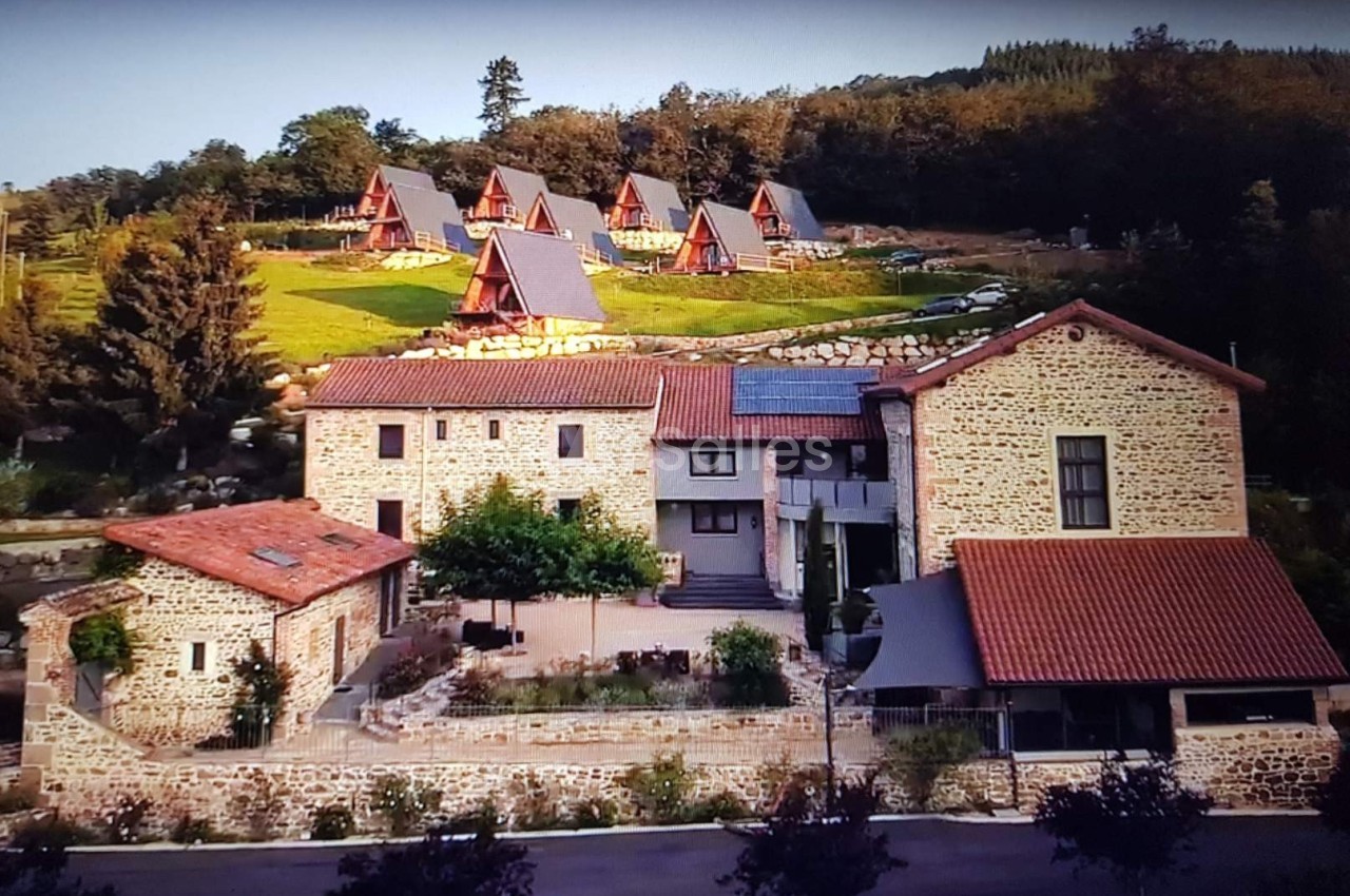 Vue d'un domaine rural avec bâtiments en pierre et chalets en bois entourés de verdure.