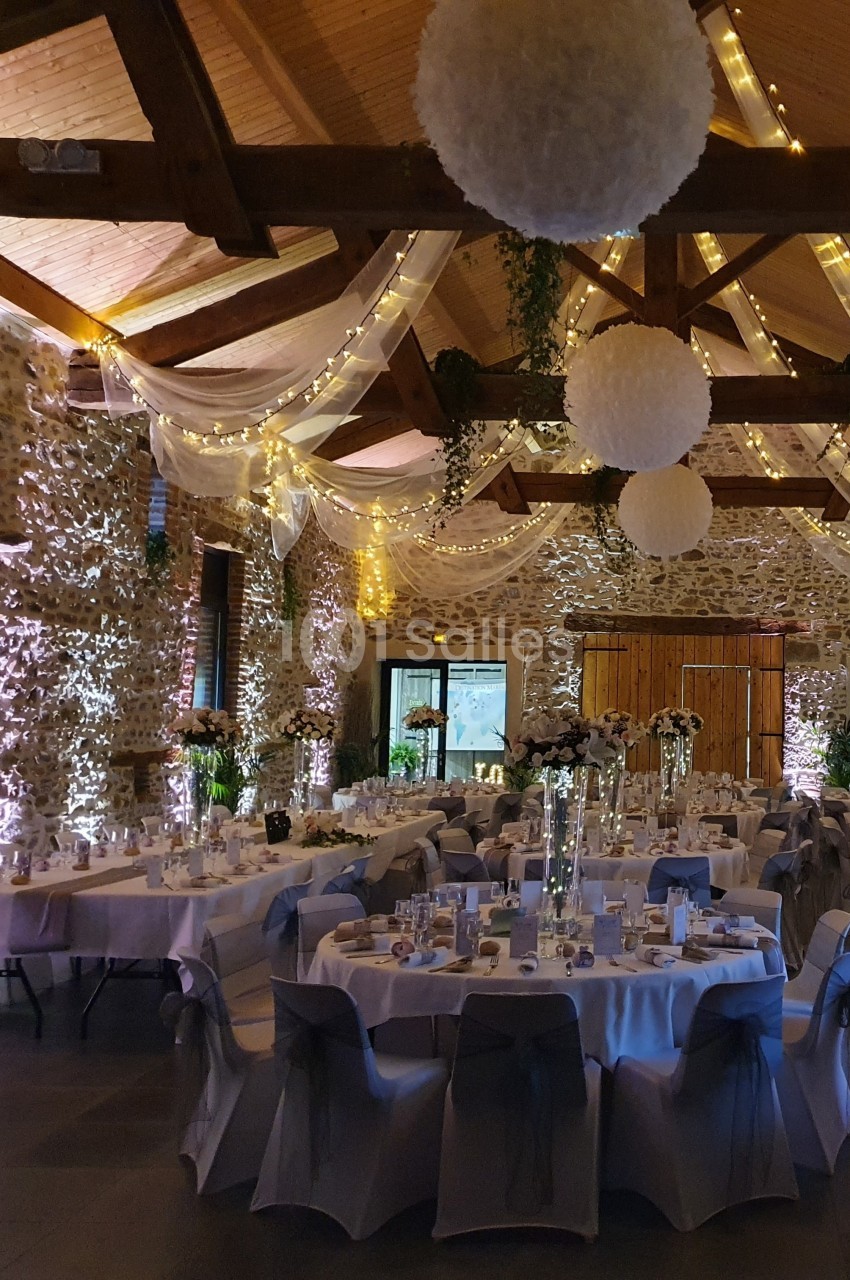 Salle de réception décorée avec des guirlandes lumineuses, des tables rondes dressées et des suspensions blanches.