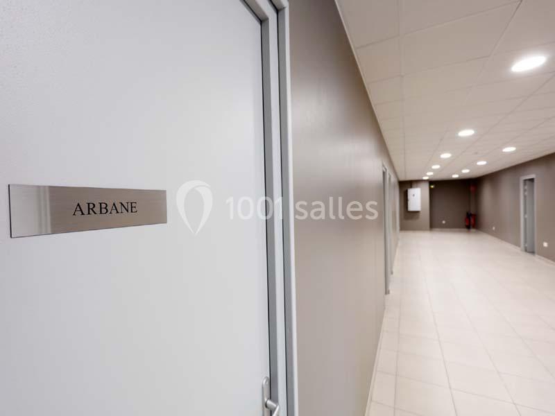 Porte avec une plaque portant l'inscription ’Arbane’ dans un couloir lumineux aux murs et sol clairs.