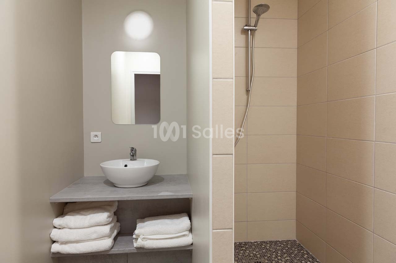 Salle de bain avec lavabo, miroir, étagère contenant des serviettes pliées et douche à l'italienne carrelée.