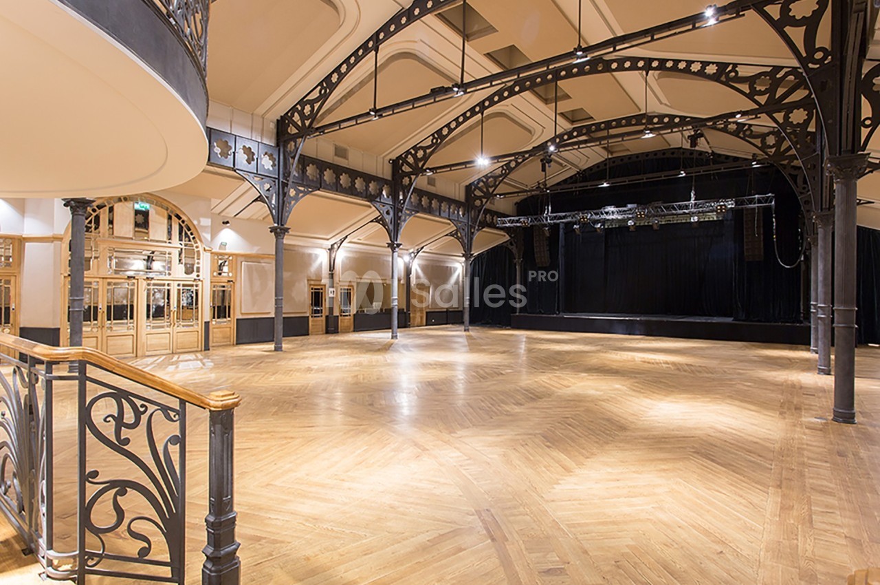 Salle spacieuse avec parquet en bois, structures métalliques décoratives et scène au fond.