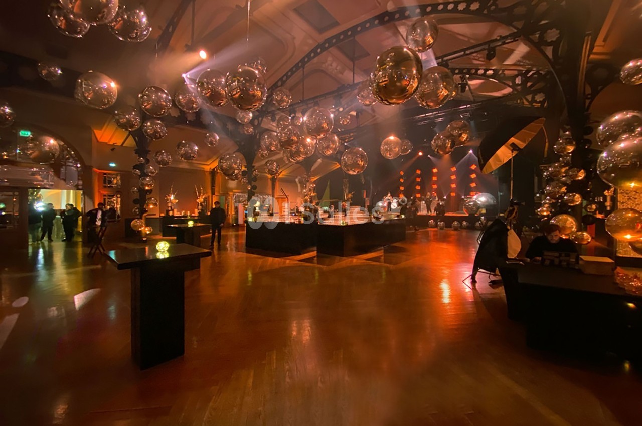 Salle de réception éclairée avec des lumières chaudes, décorée de sphères suspendues et de tables disposées autour.