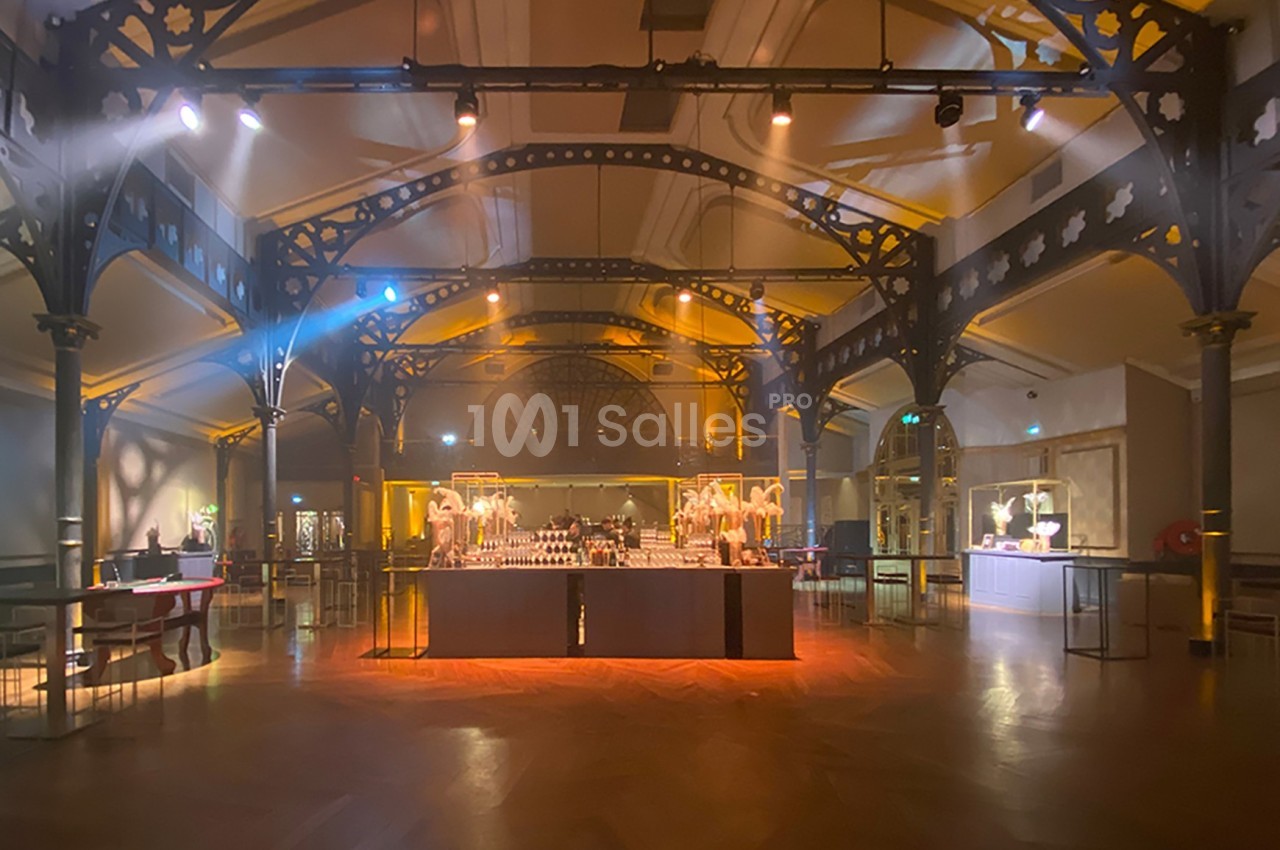 Salle lumineuse avec structure métallique, parquet en bois et tables disposées pour un événement ou une réception.