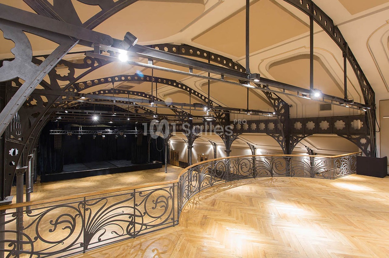 Balcon intérieur d'une salle de spectacle avec structure métallique ornée et parquet en bois clair.