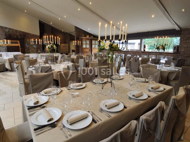Salle de réception élégamment décorée avec des tables dressées, nappes beiges et chandeliers allumés.