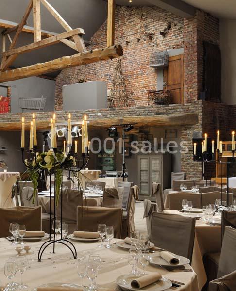 Salle de réception décorée avec des tables dressées, chandeliers allumés et murs en briques apparentes.