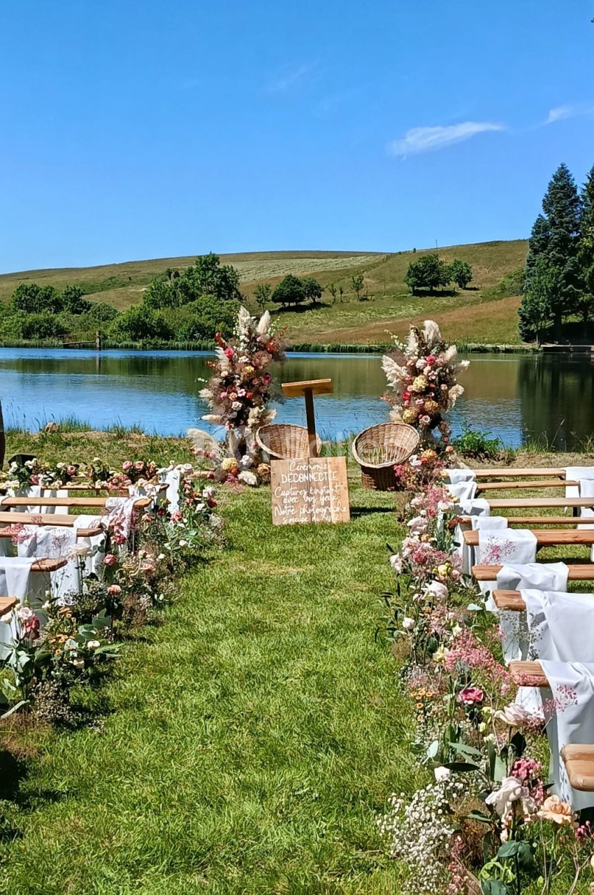 Allée décorée de fleurs menant à un autel en plein air près d'un lac, entouré de collines verdoyantes.