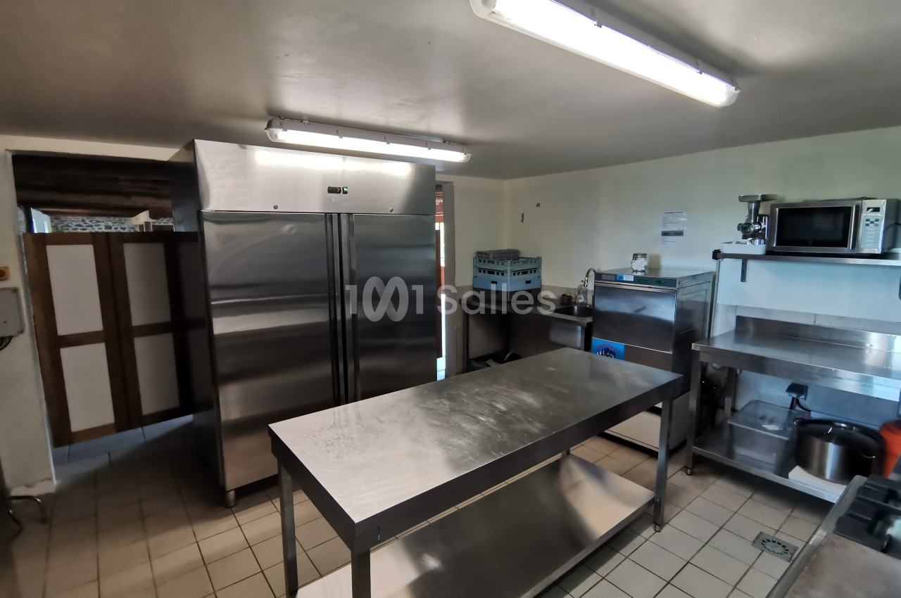 Cuisine professionnelle équipée avec plan de travail en inox, réfrigérateurs, micro-ondes et équipements divers.