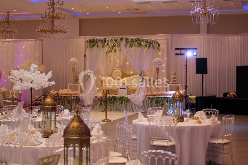Salle de réception décorée avec des tables dressées, un canapé doré sous un dais blanc et des éléments floraux.