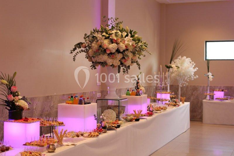 Table de buffet décorée avec des fleurs blanches et roses, éclairage violet et divers plats disposés.