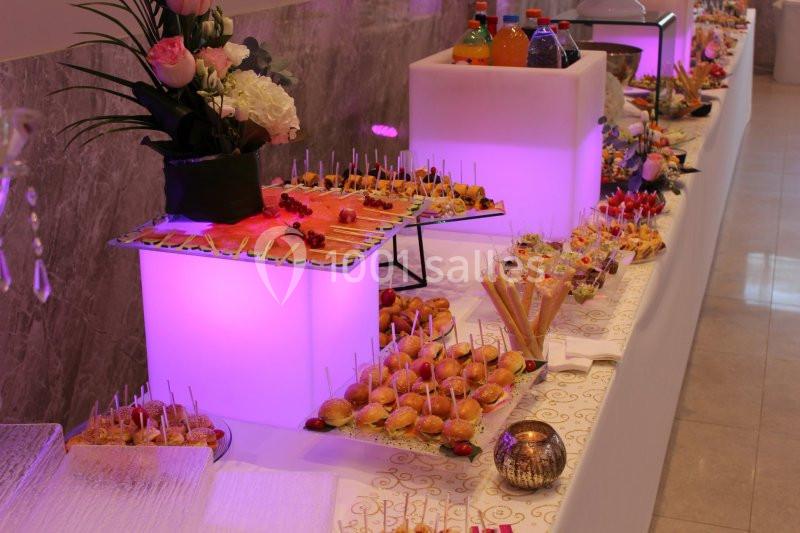Buffet lumineux avec assortiments de bouchées salées et sucrées, boissons et décorations florales.