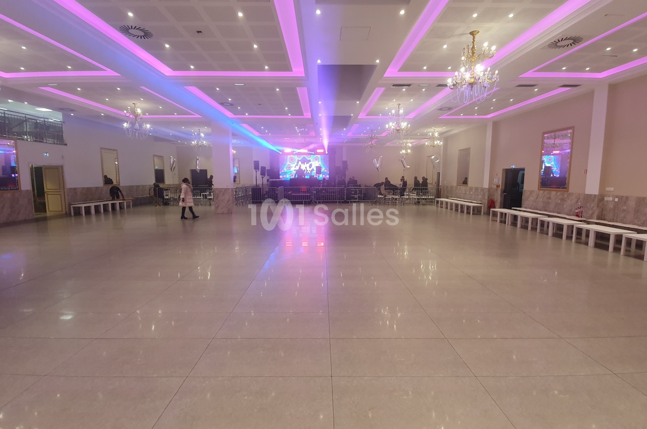 Salle spacieuse avec sol en carrelage, éclairage néon rose et blanc, scène au fond et quelques personnes présentes.