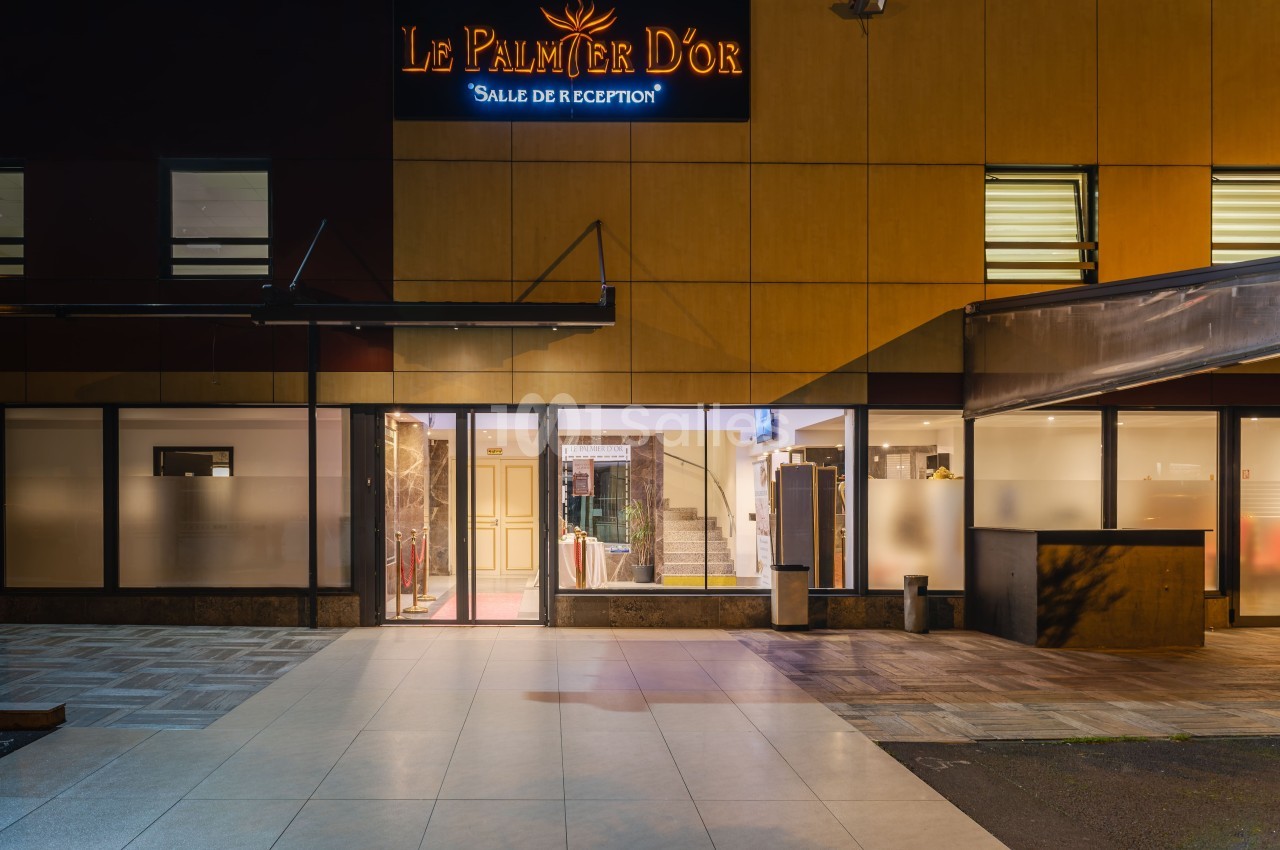 Façade éclairée d'une salle de réception avec enseigne ’Le Palmier d'Or’ visible au-dessus de l'entrée principale.