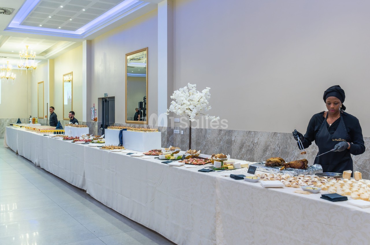 Buffet élégant avec divers plats et desserts, une serveuse en action dans une salle lumineuse et décorée.