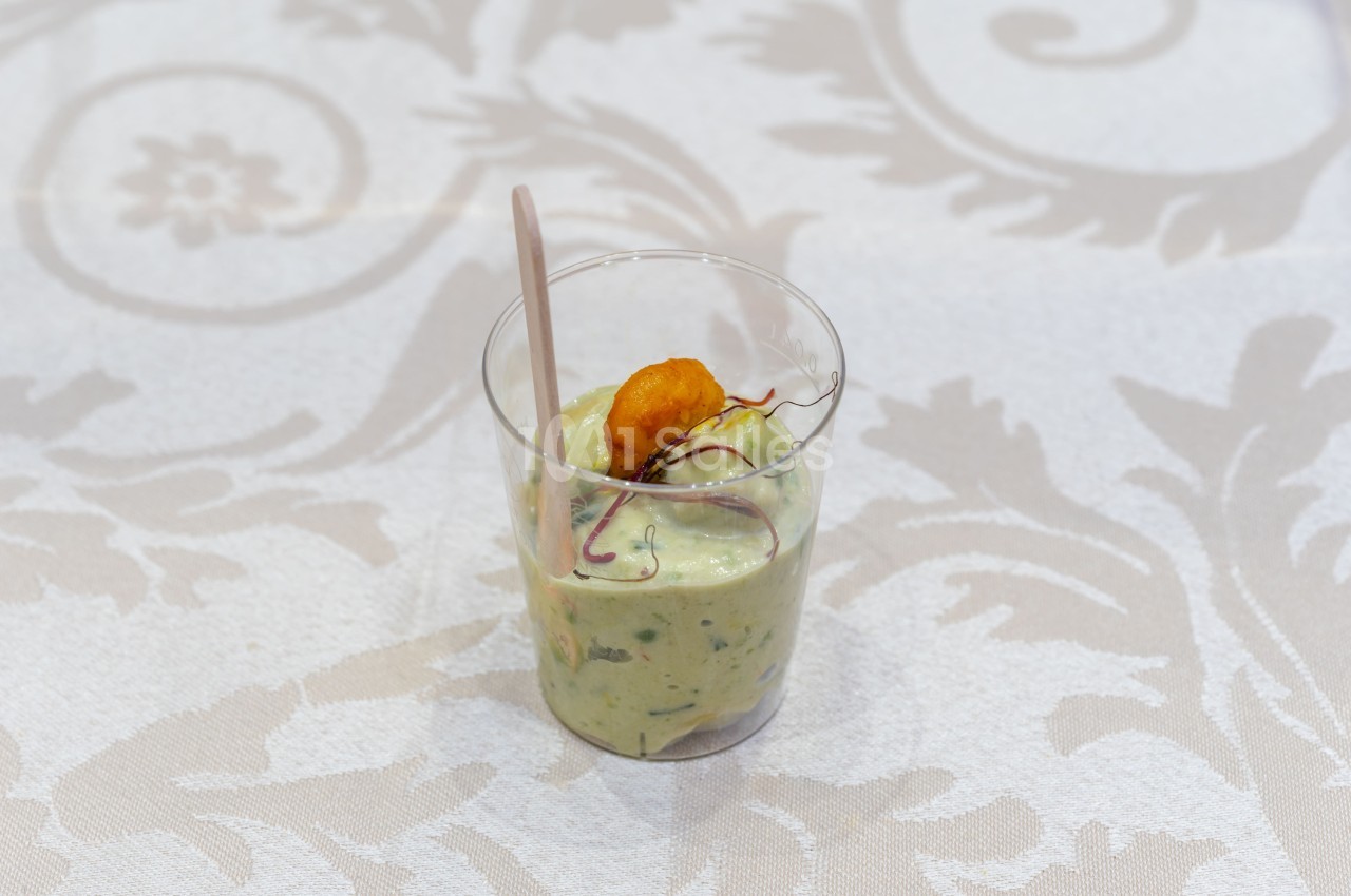 Verrine de mousse verte garnie d'une crevette et de pousses, posée sur une nappe à motifs.