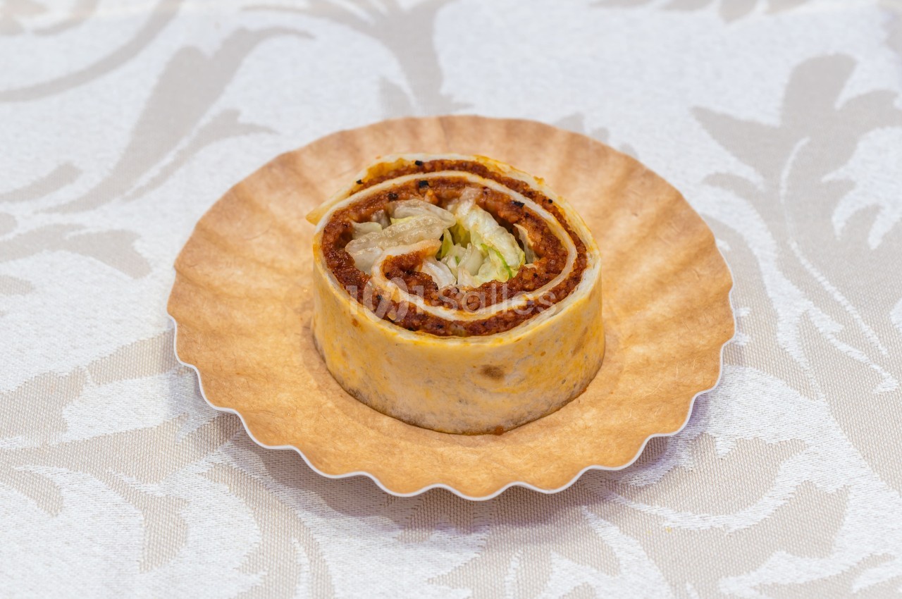Rouleau de tortilla garni de viande hachée, salade et sauce, présenté sur une assiette en papier.