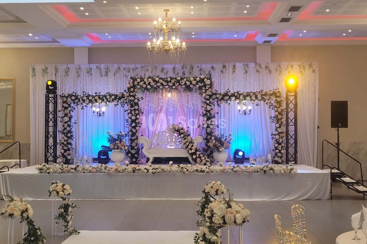 Décoration de scène de mariage avec fleurs blanches, éclairage coloré et chaises transparentes dans une salle élégante.