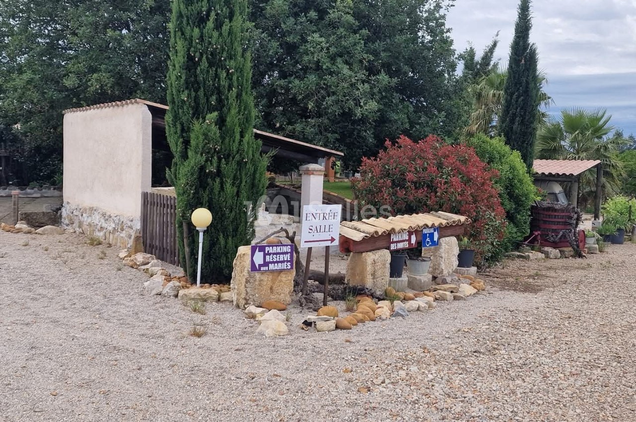 Entrée d'un domaine rural avec panneaux directionnels, végétation méditerranéenne et chemin en gravier.