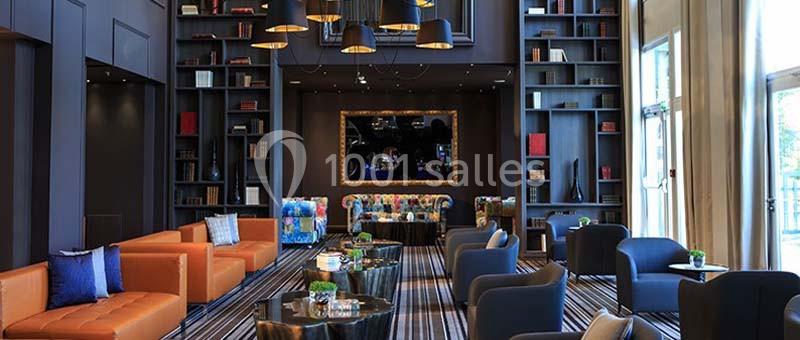 Salon moderne avec canapés colorés, fauteuils noirs, étagères remplies de livres et éclairage suspendu.