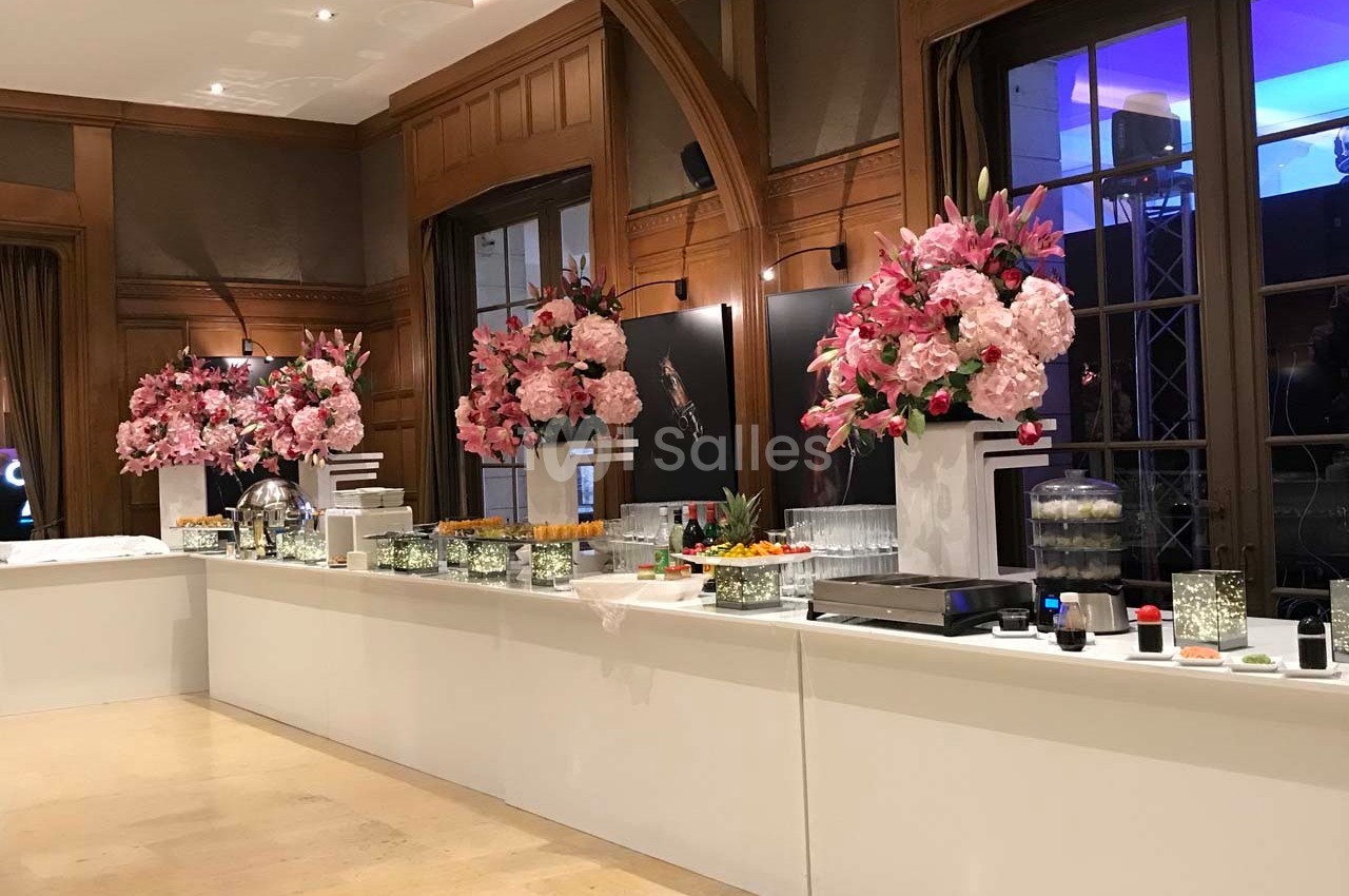 Buffet élégant avec décorations florales roses, plats variés et verrerie dans une salle aux boiseries raffinées.